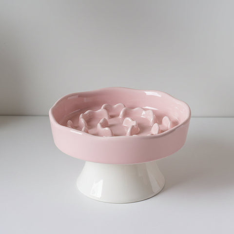 Pink ceramic elevated slow-feeder bowl with a raised flower-shaped maze center and white pedestal base on a light background.